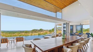 Uma sala de jantar moderna com uma mesa de madeira comprida, cadeiras confortáveis e vista para a paisagem.