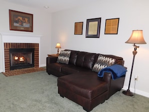 Ein Wohnzimmer mit Kamin, einem Ledersofa, einem Beistelltisch mit Lampe und drei gerahmten Zertifikaten an der Wand.