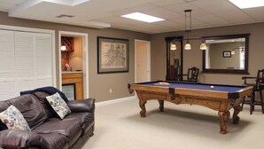 Une table de billard dans une pièce où se trouvent un canapé en cuir marron, une carte encadrée accrochée au mur et un miroir au-dessus de la table.