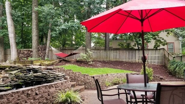 Une terrasse agrémentée d’une cascade en pierre, d’un parasol rouge et d’une table avec des chaises.