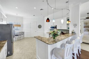 Una cocina moderna con encimera de granito, armarios blancos y un comedor con sillas blancas.