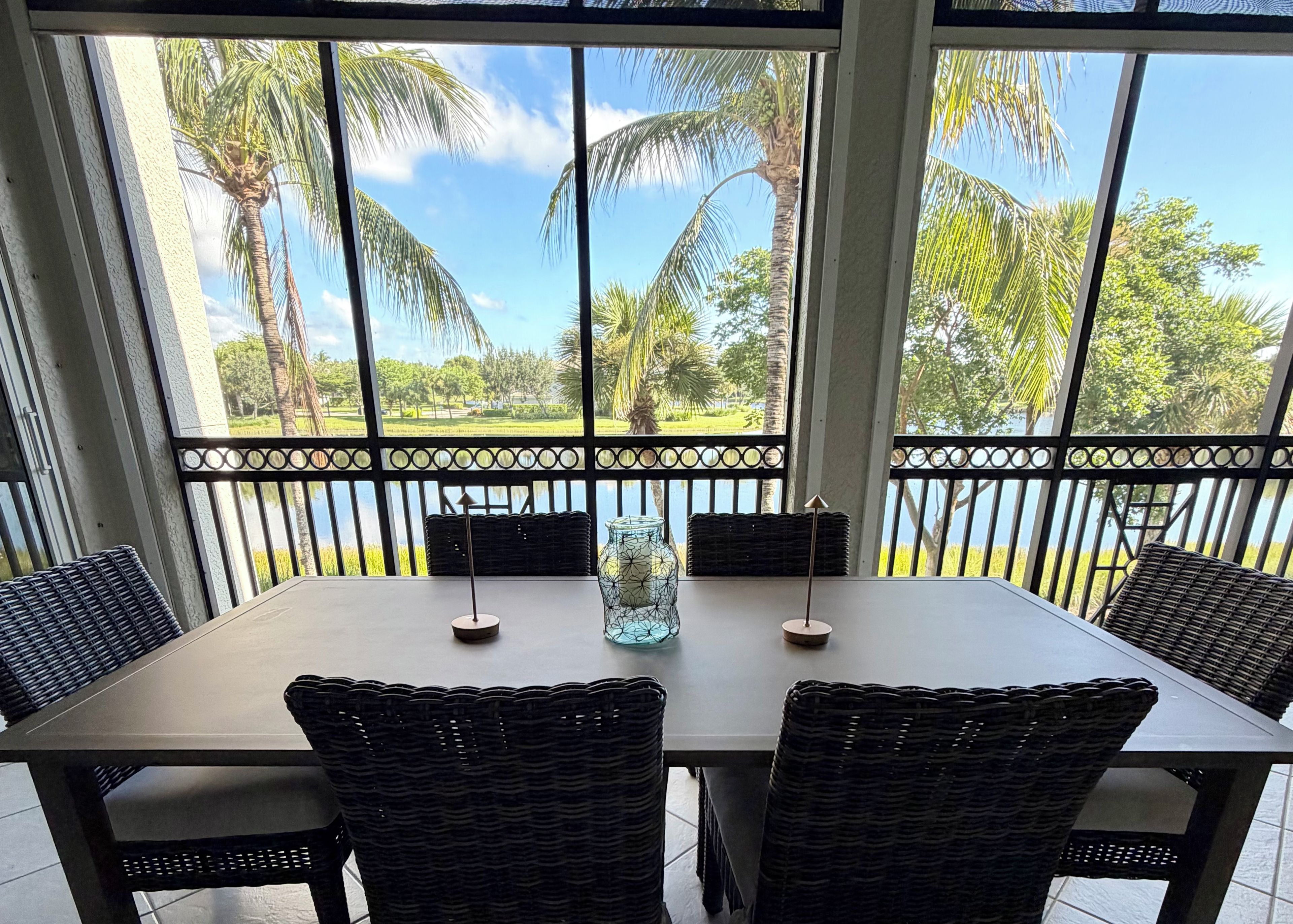 A dining area with a table and chairs, a vase, and a view of palm trees and a body of water.