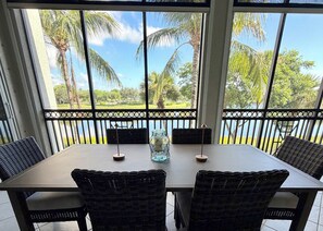 A dining area with a table and chairs, a vase, and a view of palm trees and a body of water. - Resort Style Living. Beautiful Coastal Inspired Coach Home in Fiddler’s Creek. (Naples)