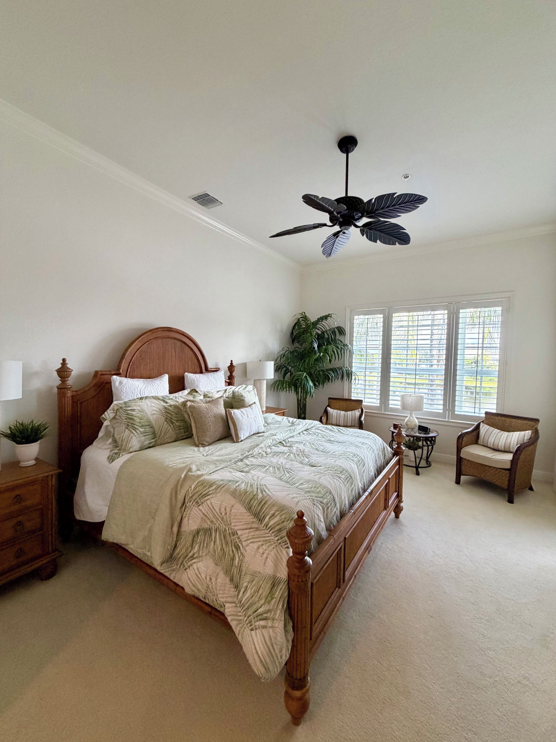 A bedroom with a wooden bed, a ceiling fan, a window with blinds, a potted plant, and a chair.