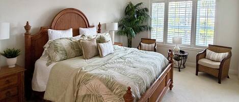 A bedroom with a wooden bed, a ceiling fan, a window with blinds, a potted plant, and a chair.