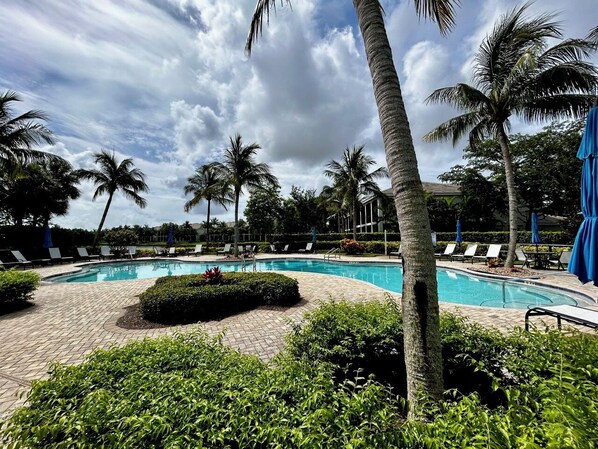 Área de piscina com espreguiçadeiras, palmeiras e céu claro.