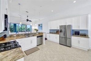A modern kitchen with white cabinets, stainless steel appliances, and a granite countertop. - Resort Style Living. Beautiful Coastal Inspired Coach Home in Fiddler’s Creek. (Naples)