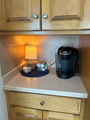 A kitchenette with wooden cabinets, a coffee maker, a lamp, and a basket of coffee pods. - Lakefront Paradise on Lake Hickory’s Main Channel – Handicap Accessible (Taylorsville)