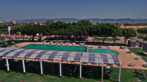 A swimming pool with a covered area and lounge chairs, surrounded by trees and a view of distant mountains.
