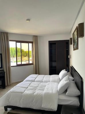 A hotel room with a large bed, a TV, and a view of greenery outside.