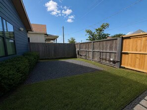 A residential backyard with a wooden fence, a gravel path, and artificial grass. - Central Houston Bungalow Cowboy Pool & EV Charger (Houston)