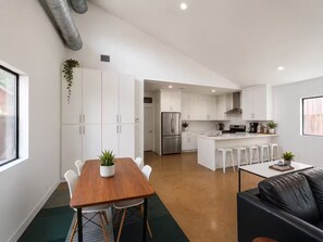 A modern kitchen with white cabinets, stainless steel appliances, and a central island with bar stools. - Central Houston Bungalow Cowboy Pool & EV Charger (Houston)