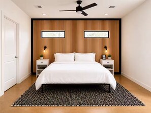 Ein modernes Schlafzimmer mit einem großen Bett, einer Wandpaneele aus Holz, zwei Nachttischen mit Lampen und einem Deckenventilator.