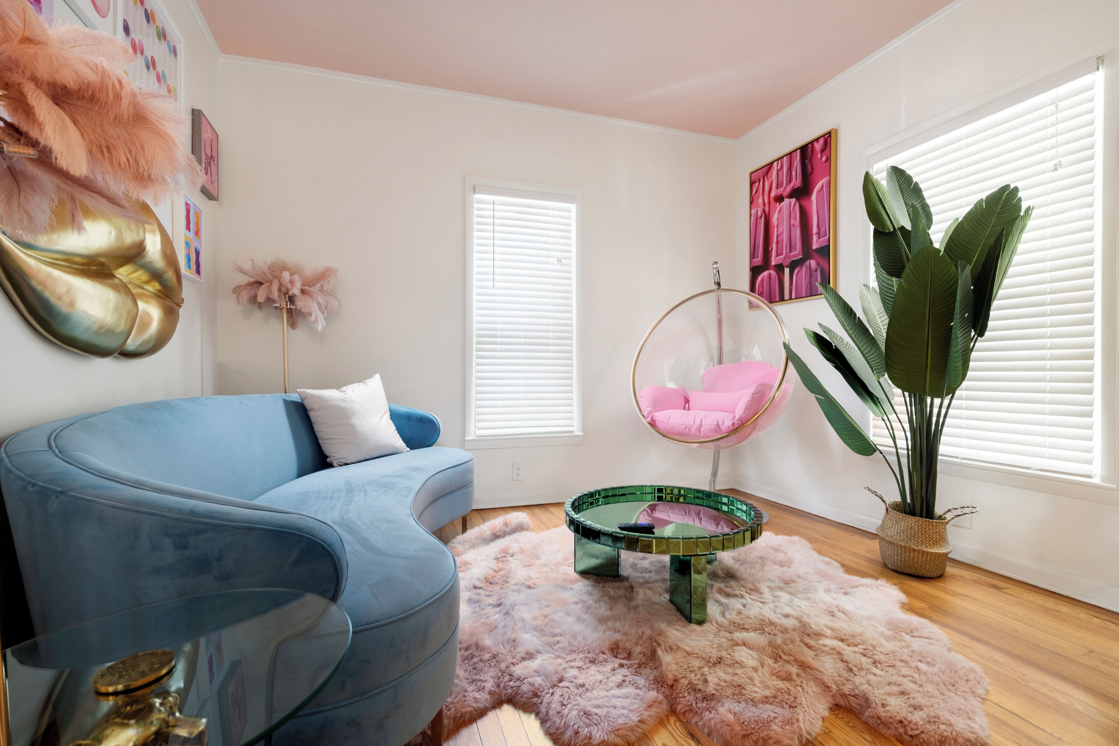 Een moderne woonkamer met een blauwe bank, een hangstoel, een ronde salontafel, een zacht vloerkleed en een grote plant.