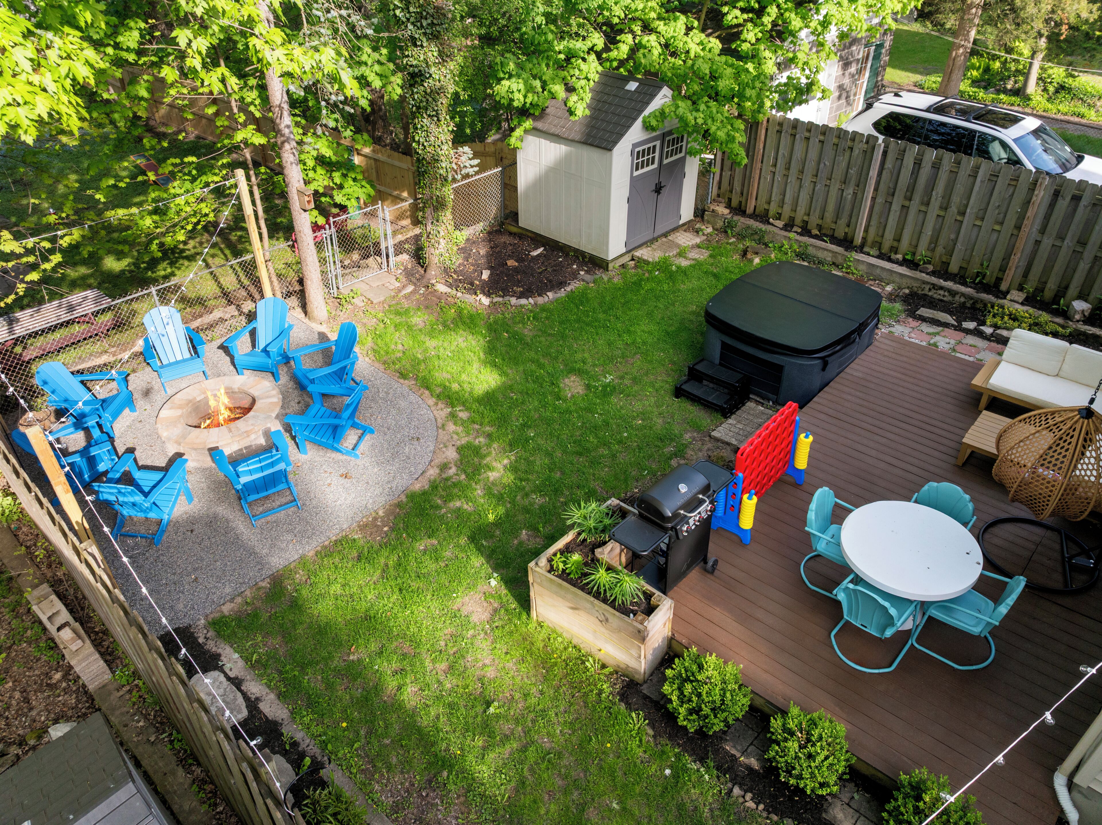A backyard with a fire pit, blue Adirondack chairs, a wooden deck, and a hot tub.