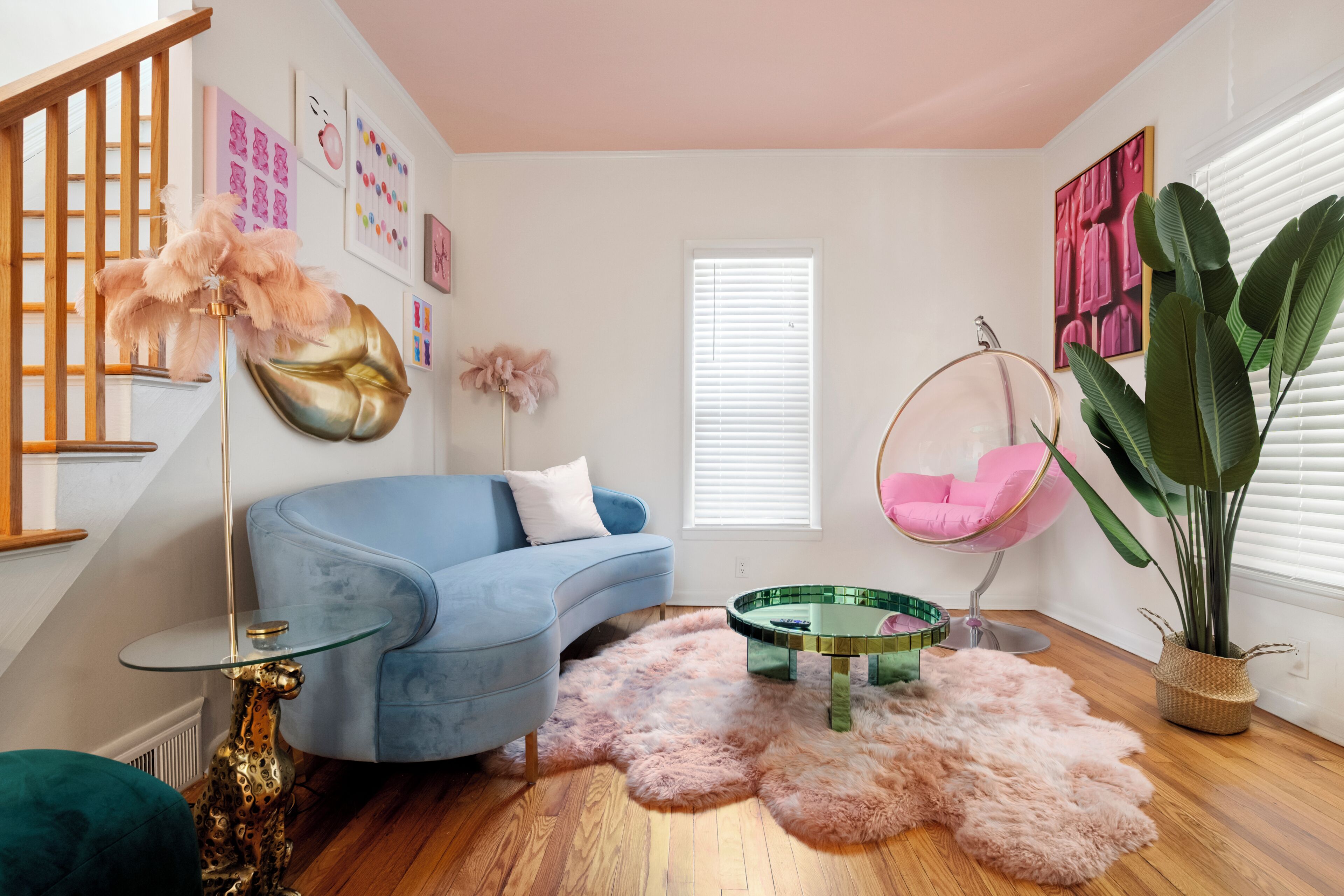 Ein modernes Wohnzimmer mit einem blauen Sofa, einem Glastisch, einem Hängekorbstuhl, einem flauschigen Teppich und einer großen Pflanze.