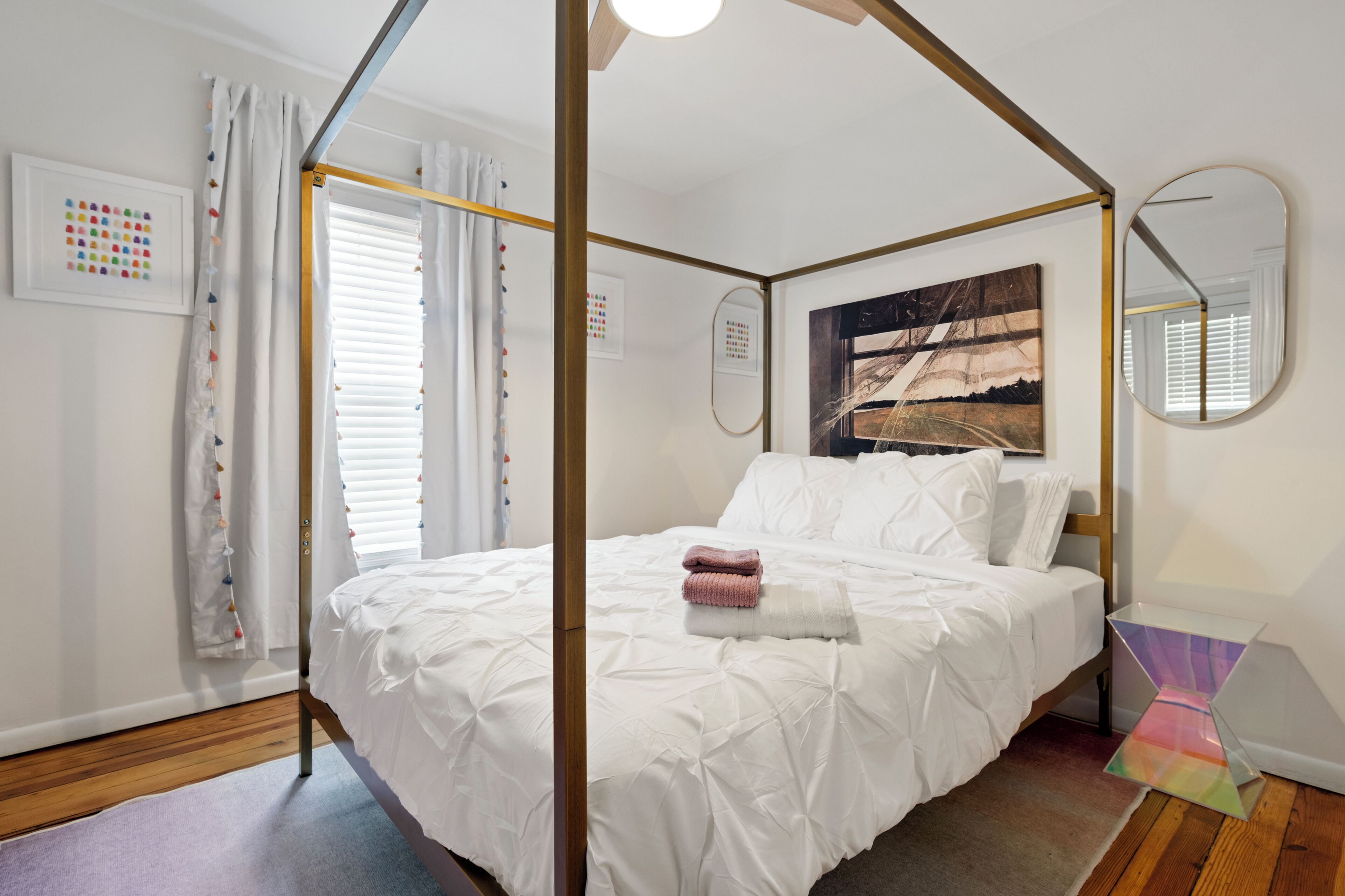 A four-poster bed with white bedding, a large mirror, and artwork on the wall.