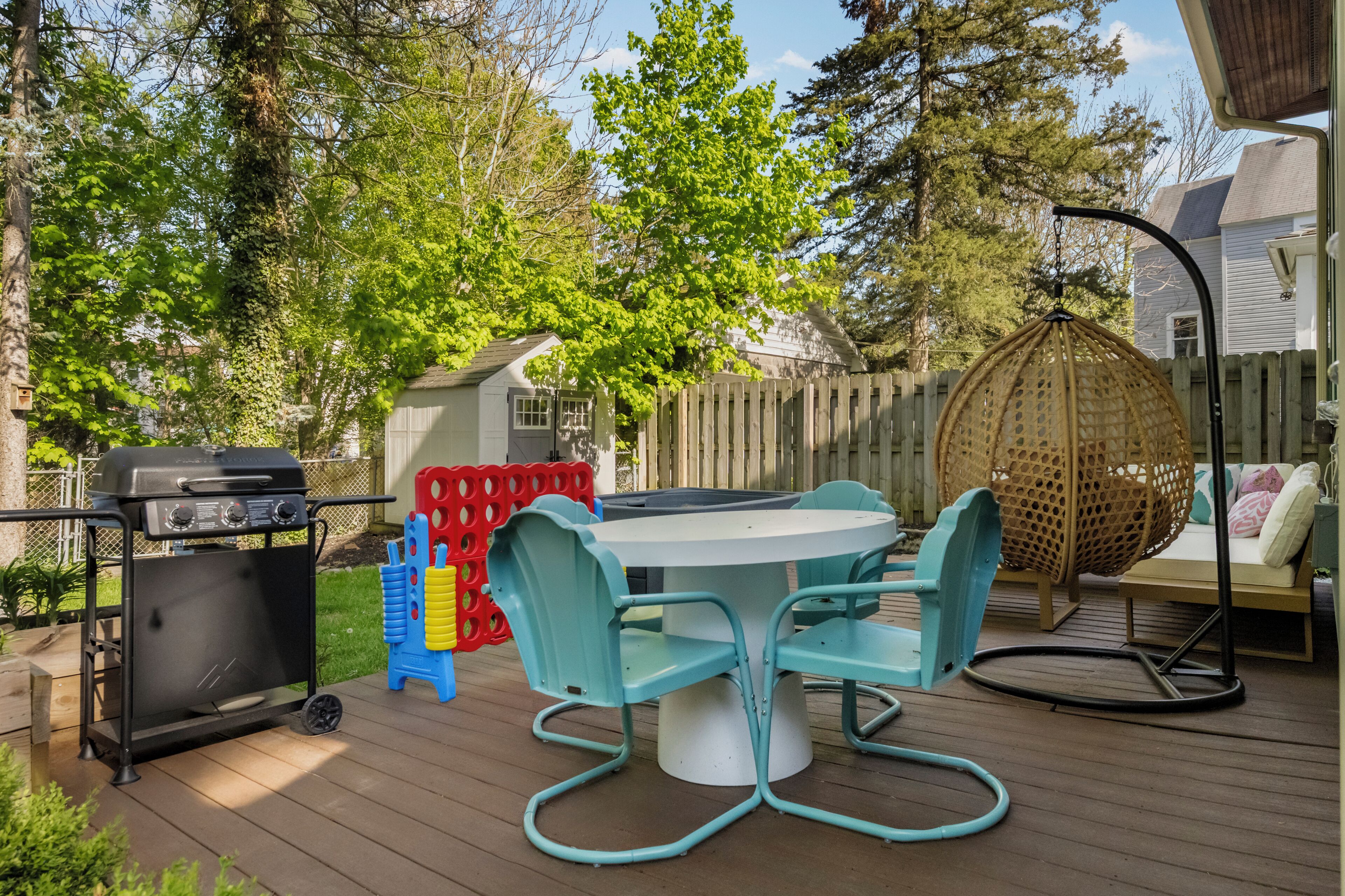 A wooden deck with a grill, a round table with chairs, a swing, and a small shed.