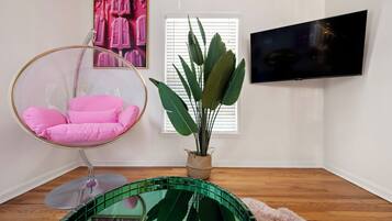 A room with a hanging chair, a potted plant, a television, and a window with blinds.