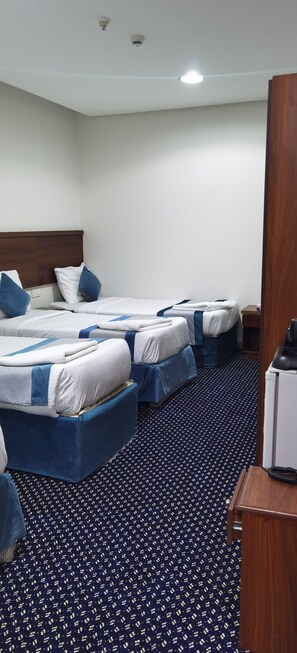 A hotel room with three beds, a desk, and a telephone.
