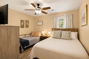 A hotel room with a bed, two bedside tables, a ceiling fan, a TV, and artwork on the walls. - Coastal Chic Golf Retreat Fairways 18F (Myrtle Beach)