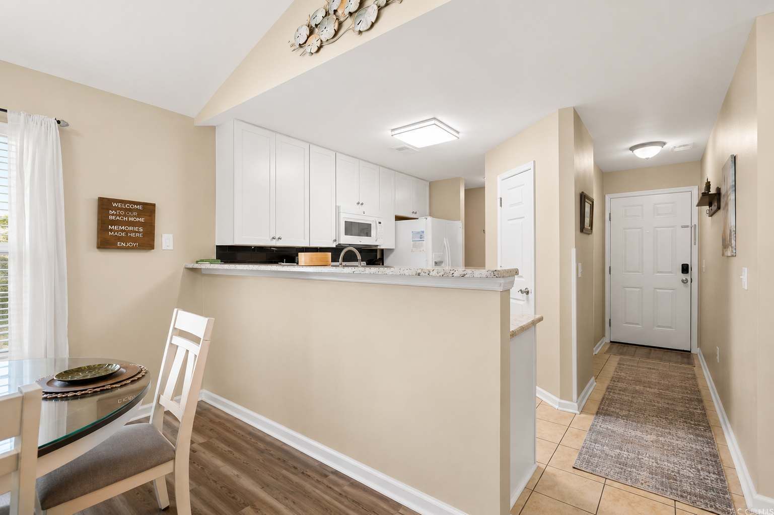 A kitchen with white cabinets, a microwave, and a wooden countertop. There is a dining table with chairs and a sign on the wall.