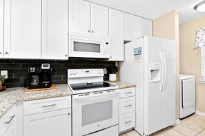 A kitchen with white cabinets, a microwave, a stove, a refrigerator, and a coffee maker. - Coastal Chic Golf Retreat Fairways 18F (Myrtle Beach)