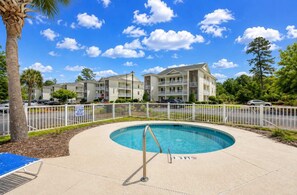 A pool area with a lifeguard stand, a fenced pool, and a multi-story building in the background. - Coastal Chic Golf Retreat Fairways 18F (Myrtle Beach)