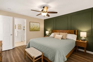 A bedroom with a bed, a nightstand, a bedside lamp, a ceiling fan, a door, and a wall with a picture. - Coastal Chic Golf Retreat Fairways 18F (Myrtle Beach)