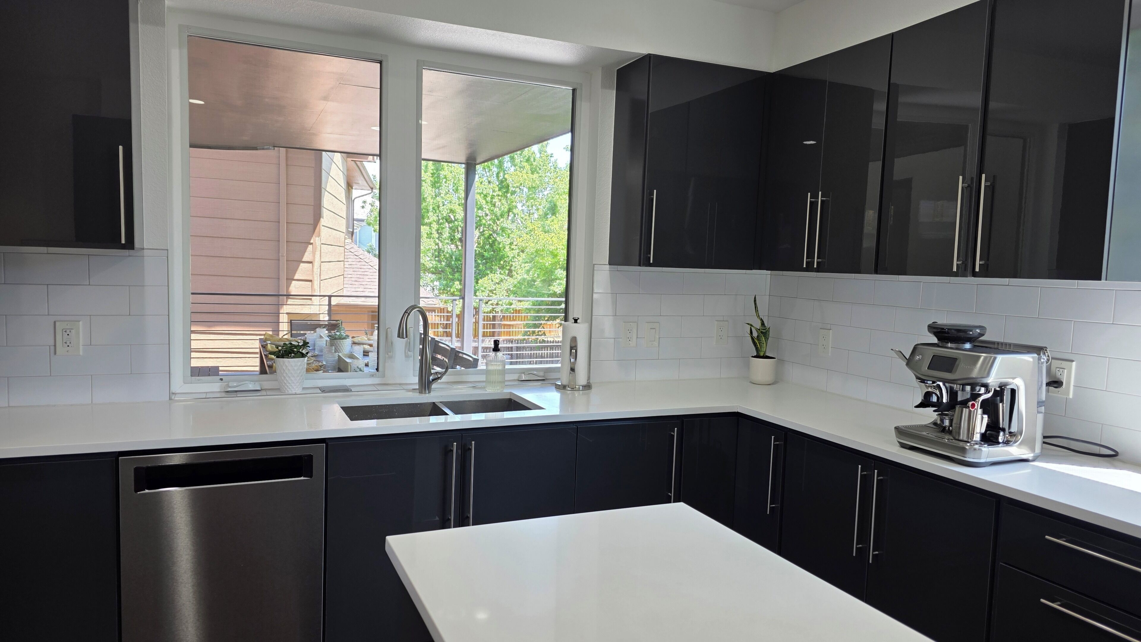 A modern kitchen with black cabinets, a white countertop, a stainless steel dishwasher, and a coffee maker.