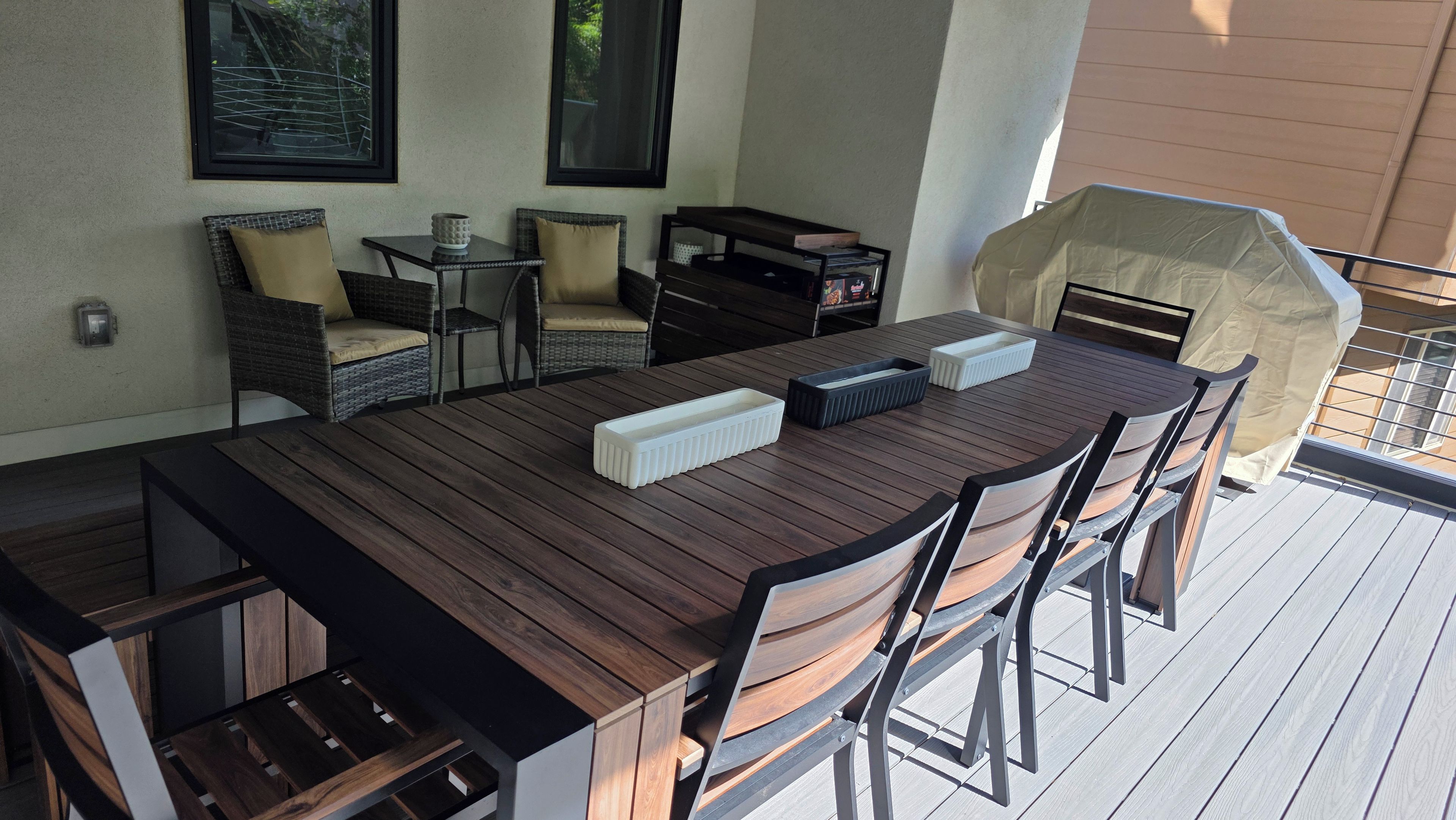 Een terras met een houten tafel, stoelen en een barbecue.
