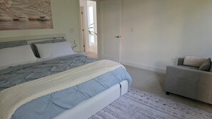 A bedroom with a bed, a sofa, a patterned rug, and a door leading to another room.