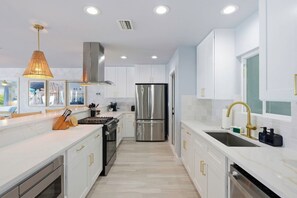 A modern kitchen with white cabinets, stainless steel appliances, and a large window. - Private Dock • Pool • Hot Tub • Puttputt • Games (St. Petersburg)