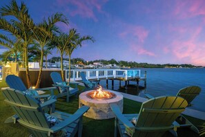 A deck with chairs and a fire pit overlooking a body of water. - Private Dock • Pool • Hot Tub • Puttputt • Games (St. Petersburg)