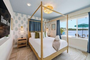 A bedroom with a four-poster bed, a nightstand, a wall-mounted lamp, a view of the sea, and a 'Home Team' sign. - Private Dock • Pool • Hot Tub • Puttputt • Games (St. Petersburg)