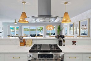 A modern kitchen with a central stove, overhead lighting, and large windows offering a view of the sea. - Private Dock • Pool • Hot Tub • Puttputt • Games (St. Petersburg)