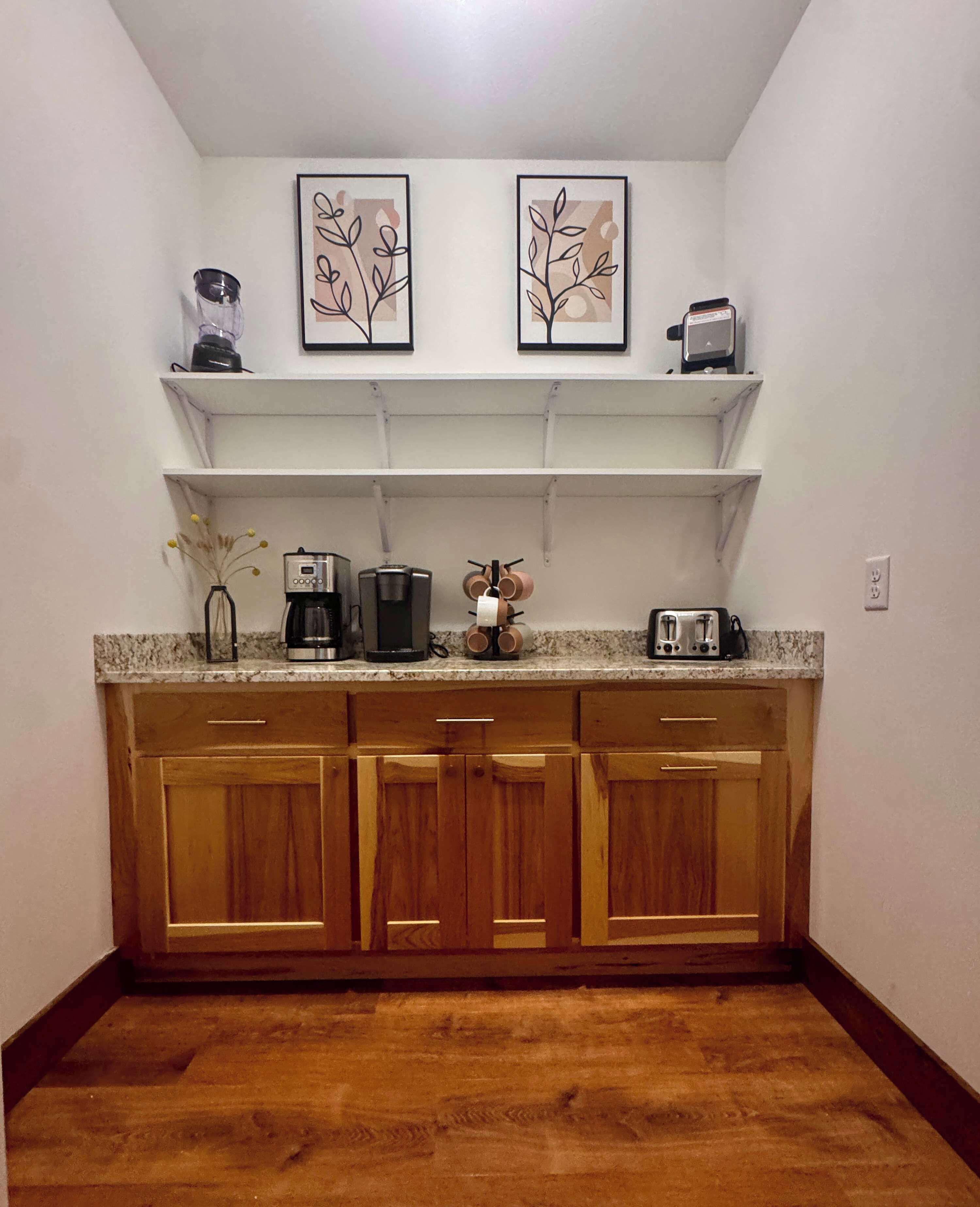 Una cucina con mobili in legno, un piano di lavoro, una macchina da caffè, un tostapane e due quadri appesi al muro.