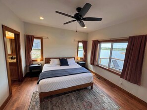 Ein Schlafzimmer mit einem Bett, zwei Nachttischen, einem Deckenventilator und großen Fenstern mit Vorhängen.