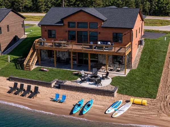 Una casa a due piani in legno con veranda, posti a sedere all'aperto e kayak su una spiaggia.