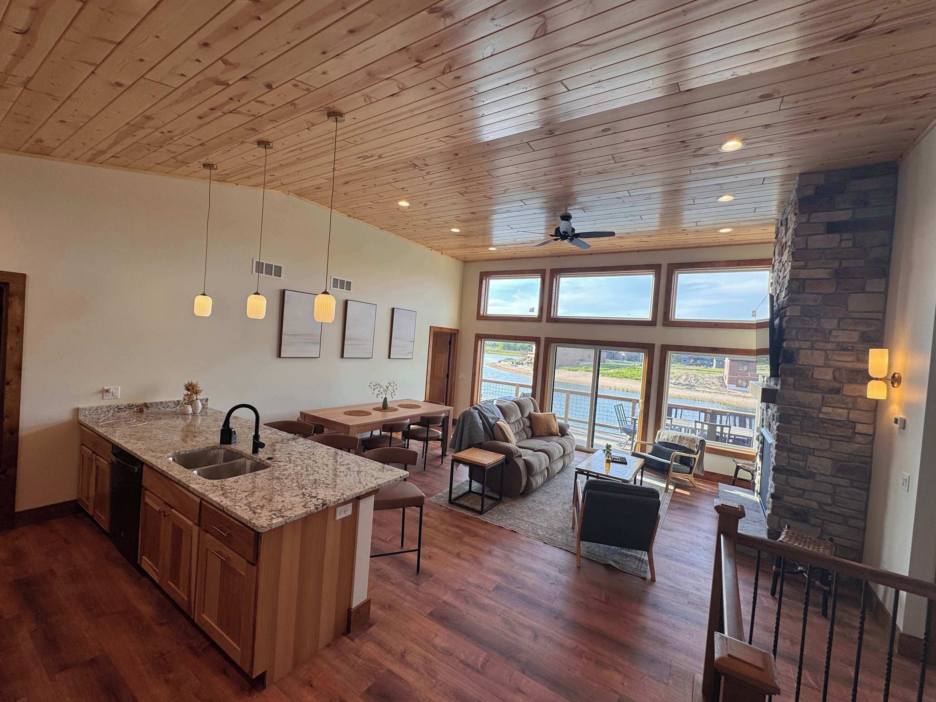 A spacious kitchen with a large island, wooden ceiling, and large windows overlooking a scenic view.