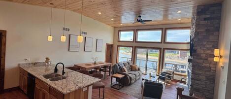 A spacious kitchen with a large island, wooden ceiling, and large windows overlooking a scenic view.