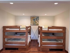 A room with two bunk beds, wooden flooring, a painting on the wall, and recessed ceiling lights. - Sugar Sand Sunset | Beachfront | Sleeps 20 (New Lisbon)