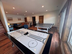 A room with a ping pong table, a foosball table, and a sofa in the background. - Sugar Sand Sunset | Beachfront | Sleeps 20 (New Lisbon)
