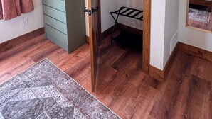 Habitació amb una porta de fusta, un armari verd, una barra de roba penjada i una catifa amb dibuixos.