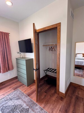 Ein Zimmer mit Holztür, einem grünen Schminktisch, einem Kleiderständer und einem gemusterten Teppich.