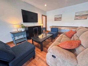 Ein Wohnzimmer mit einer Couch, Sesseln, einem Couchtisch, einem Fernseher und einem Kamin.