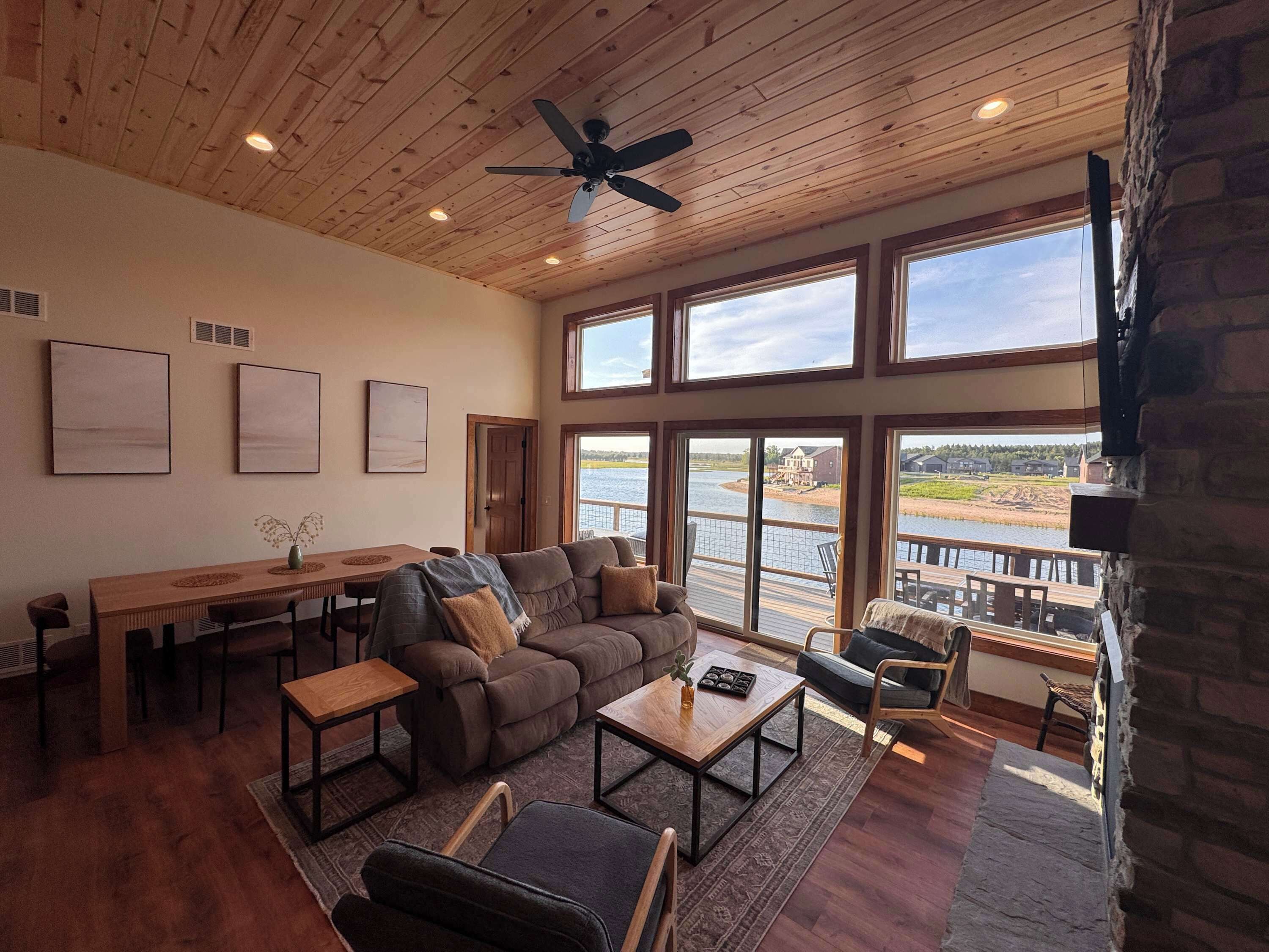 A spacious living room with a large window overlooking a body of water, a ceiling fan, and a fireplace.