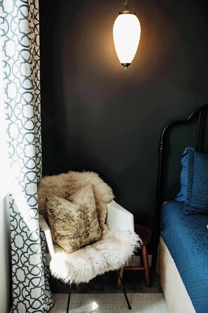 A corner of a room with a white chair, a fluffy pillow, a small stool, and a bed with a blue blanket. - Hidden Lake Escape | Hot Tub | Near Dells (Wisconsin Dells)
