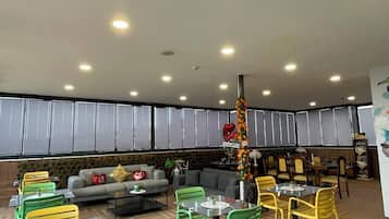 Un restaurante con varias mesas y sillas, un rincón con sofá y una columna decorativa.