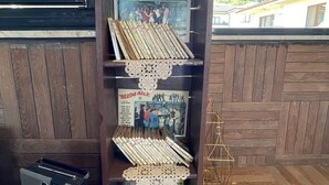 Een houten boekenkast met diverse spullen, waaronder boeken, een cassette speler en decoratieve objecten.